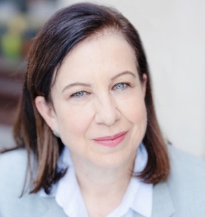 Smiling woman with long dark hair, wearing a white shirt and a light blue blazer