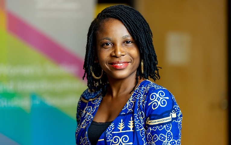Cecilia Avorkliyah A smiling woman with long braided hair, large gold hoop earrings, wearing a blue patterned shirt and a black top underneath