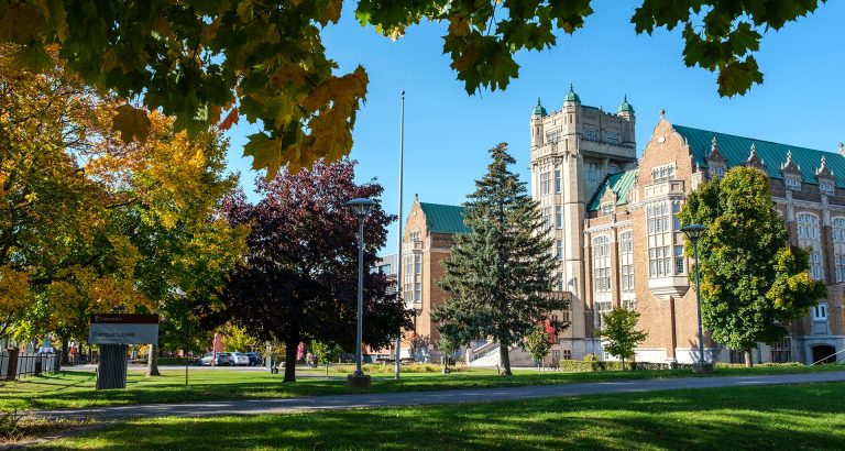 Le terrain d'une université à la fin de l'été, avec des bâtiments universitaires dans une étendue herbeuse et de grands érables dont les feuilles commencent à tourner.