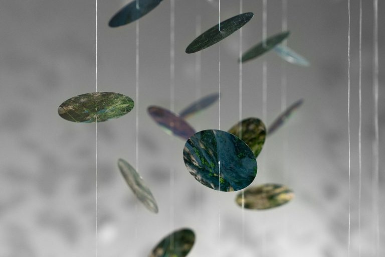 Des disques de verre colorés suspendus au plafond dans une exposition en galerie