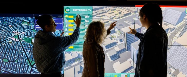 Three people standing in front of a screen featuring a graphic representation of city buildings seen from above.