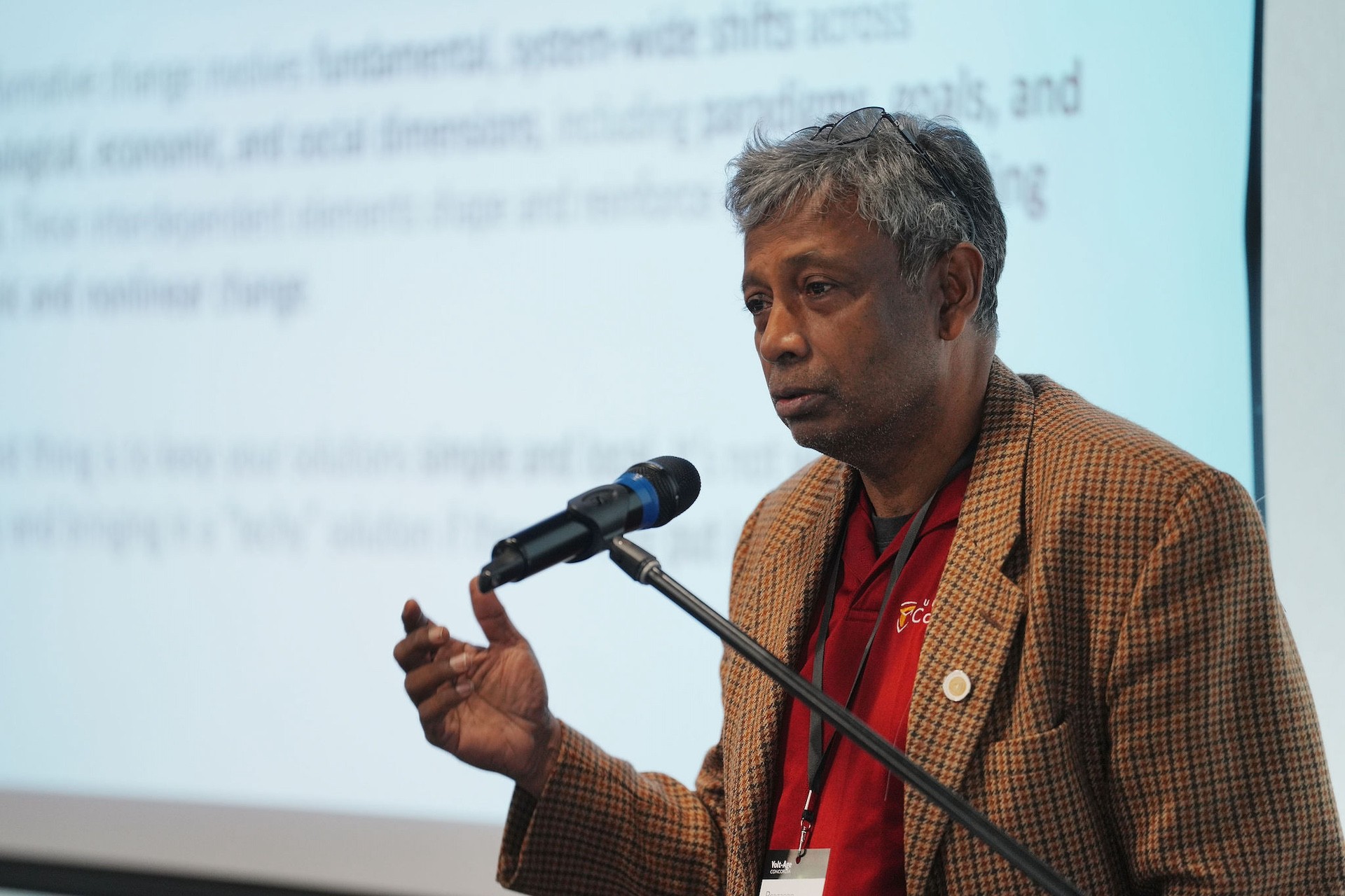  Un homme se tient devant un microphone, face à un écran blanc géant.