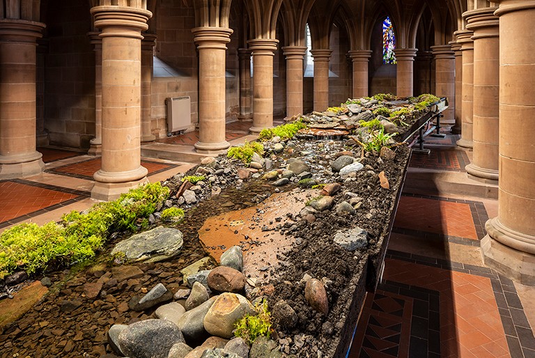 Un espace intérieur avec du carrelage, des colonnes et une installation composée de rochers et d'eau au centre