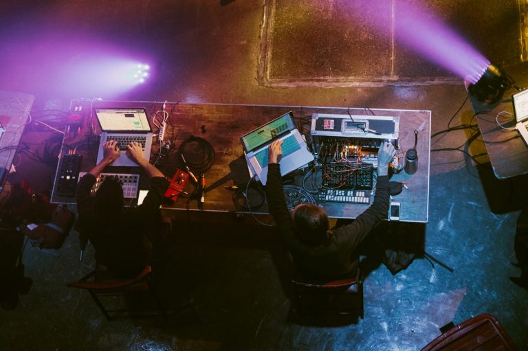 Photo de deux personnes, prise en plongée, assises à une grande table et utilisant des ordinateurs portables et des lecteurs de musique