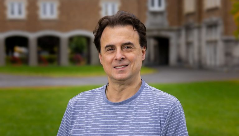 A researcher in a blue shirt standing on a sunny campus
