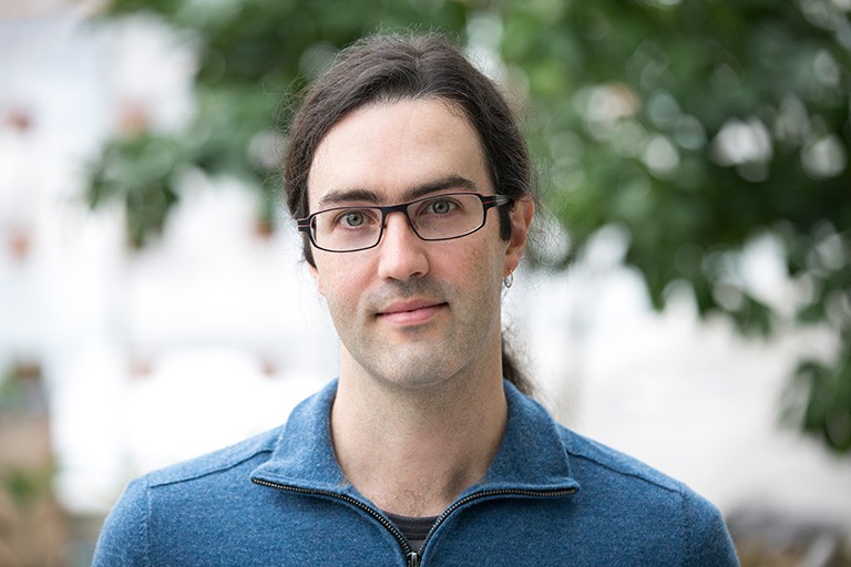 Damon Matthews, professor and Concordia Research Chair in Climate Science and Sustainability. Young man with long brown hair tied in a low ponytail, and with black-rimmed glasses.