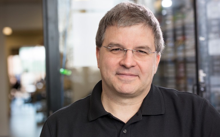 Man with short brown hair and rimless glasses, in a black polo shirt.