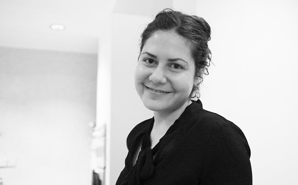 Black and white image of a smiling young woman with dark brown hair gathered loosely in a bun.