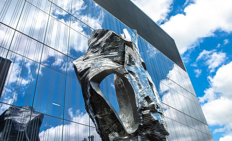 Large metal sculpture in front a building made of windows.