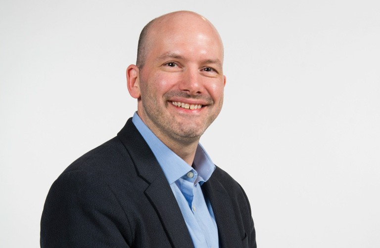 Balding, smiling man with a blue shirt and black jacket.