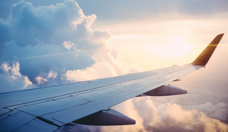 Image of the wing of a plane, with clouds in the background.