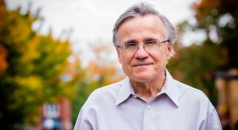 Older smiling man with short grey hair and wire frame spectacles.