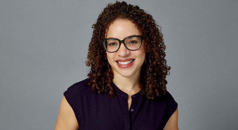 Young smiling woman with long curly hair and glasses.