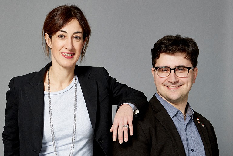 A young woman and man, smiling, in dark suit jackets.