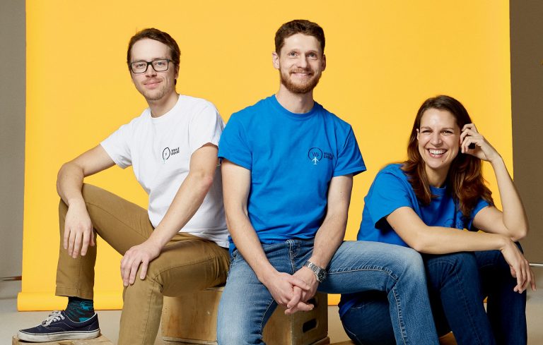 Three young people, wearing jeans and a t-shirt, sitting against a yellow background.
