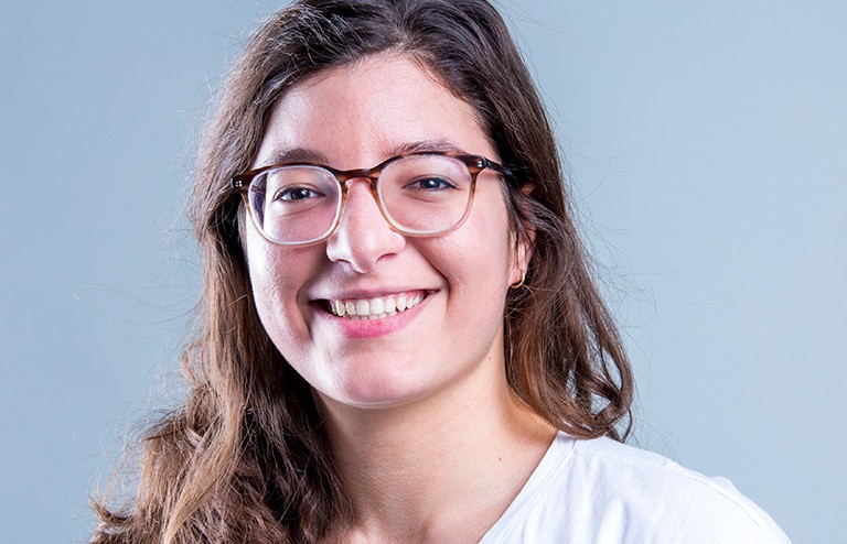 Kenza Samlali: “Microfluidic technologies, also known as lab-on-a-chip, manipulate fluids on a micro scale.” Young smiling woman with long dark hair, wearing glasses and a white T-shirt.