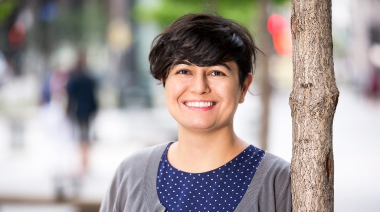 Young, smiling, woman with short, dark hair, standing in an outdoor setting.