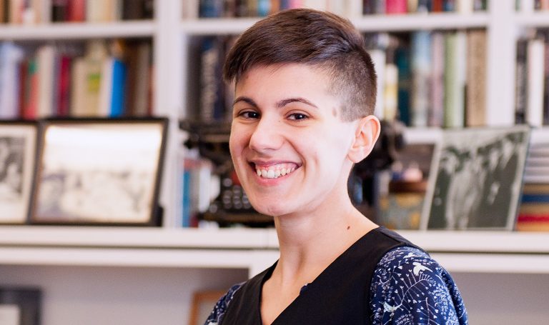 Young, smiling woman with short, dark hair, in a study or library setting.