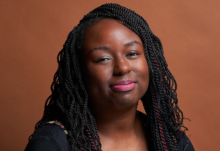 Kharoll-Ann Souffrant: "By centring those voices, I do believe that it can become beneficial for society as a whole.” Young, smiling Black woman with braids and a black top.