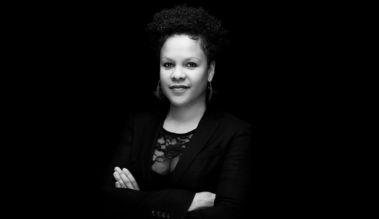 Black and white photo of a young, smiling Black woman, with her arms folded.