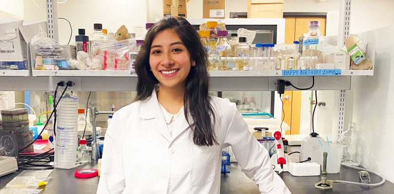 Young smiling woman dressed in a white lab coat and in a lab setting.