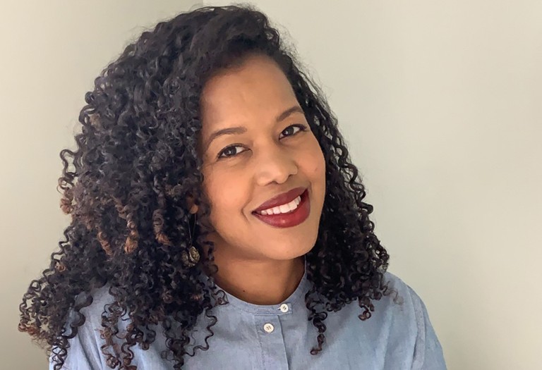 Young, black woman with long, dark curly hair, red lipstick and a blue shirt.