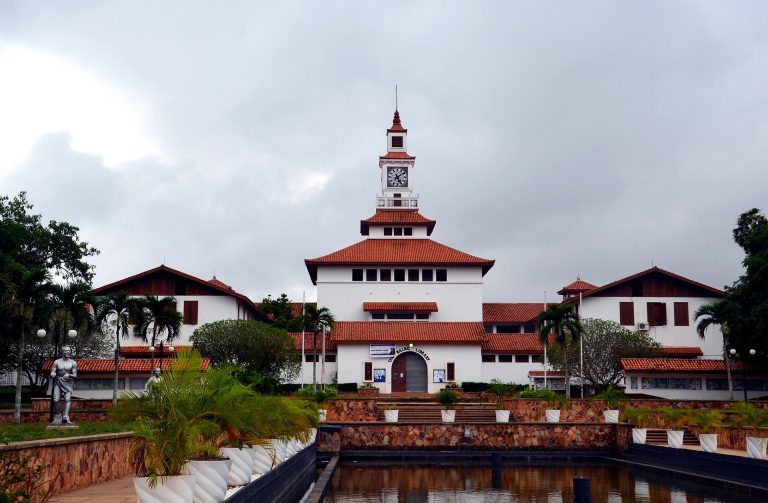 White university building with orange shingles, behind steps leading to man-made body of water.