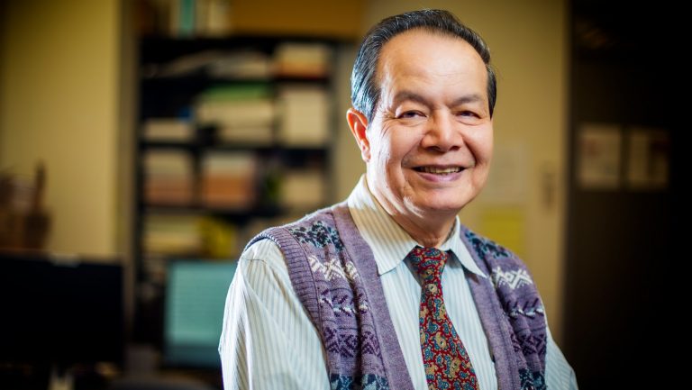 Older, smiling gentleman with a tie and knitted cardigan.