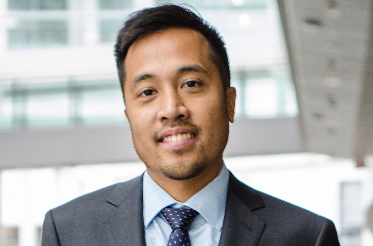 Young smiling man with short hair and a short beard, in a business suit and tie.