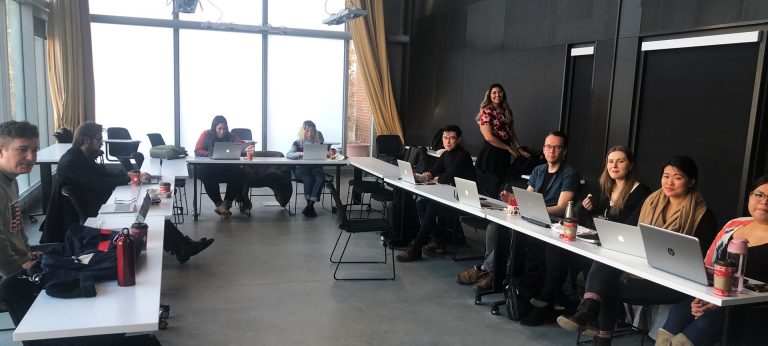 Various students with laptops seated around a large conference room table.