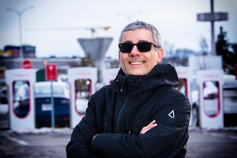 Man smiling with his arms crossed standing in front of electric car chargers