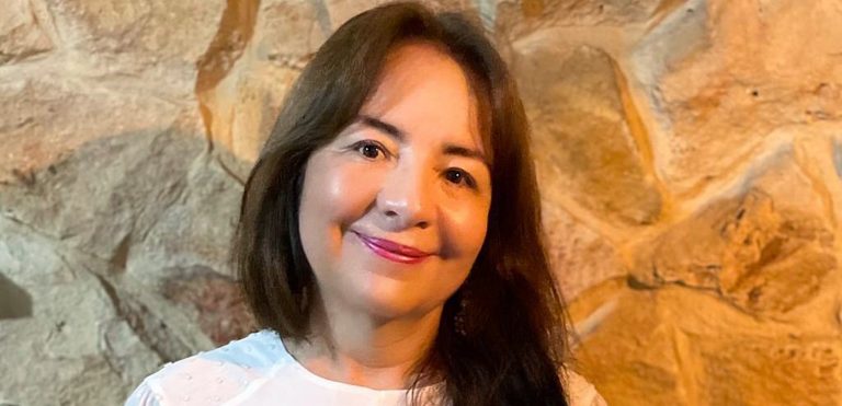 Smiling woman with long, dark hair, lipstick and a white blouse.