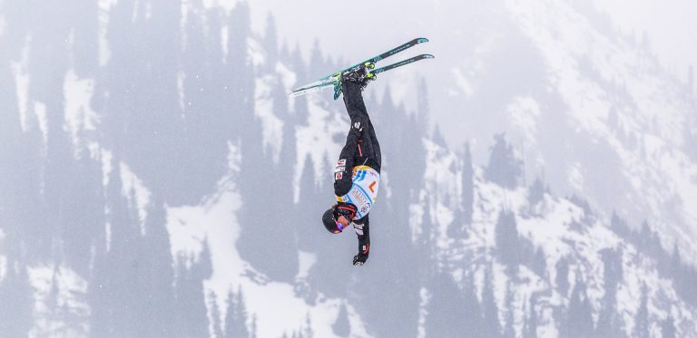 Freestyle skier in the midst of an aerial jump with snowy mountain in the background.