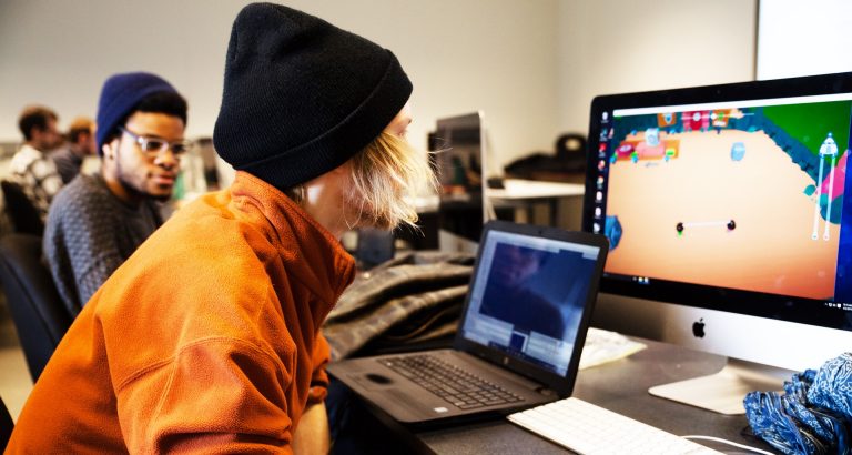 Two university students at a desk, using a desktop computer.