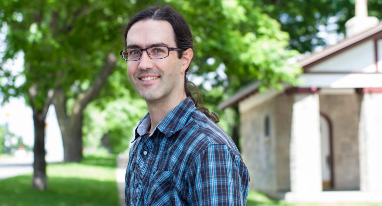 Young man with long, dark hair, glasses and a checkered shirt.