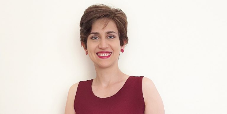 Young, smiling woman with short hair, red lipstick and a red dress.