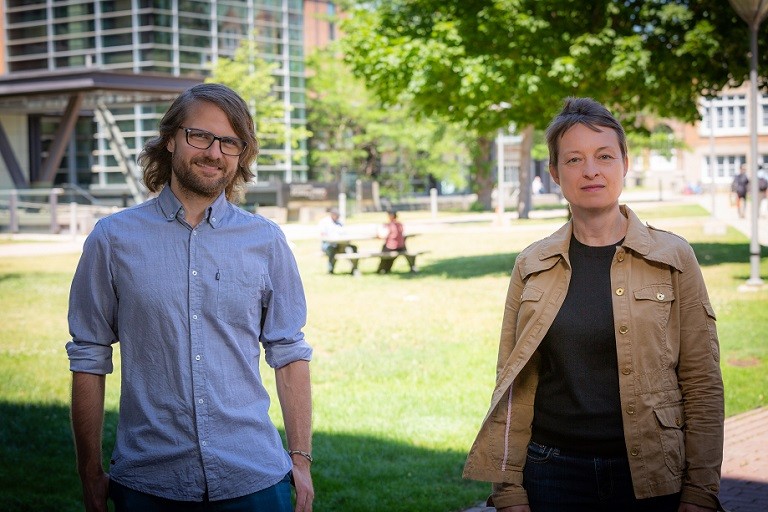Anders Bjørn and Shannon Lloyd Man with glasses in blue collared shirt and woman in brown jacket standing near a lawn