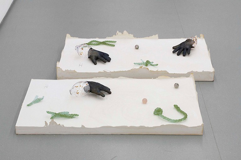 Lorna Bauer, The Hand of Mee and the Moonflower Version 3, 2019. An art installation featuring five hand blown glass vessels in stainless steel butcher gloves on a plaster base