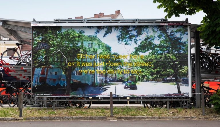 Urban setting with a billboard showing the words, "Either I was queer here, or it was just down the street, we're too early to say."