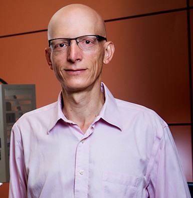 Bald man with glasses and a pink shirt.