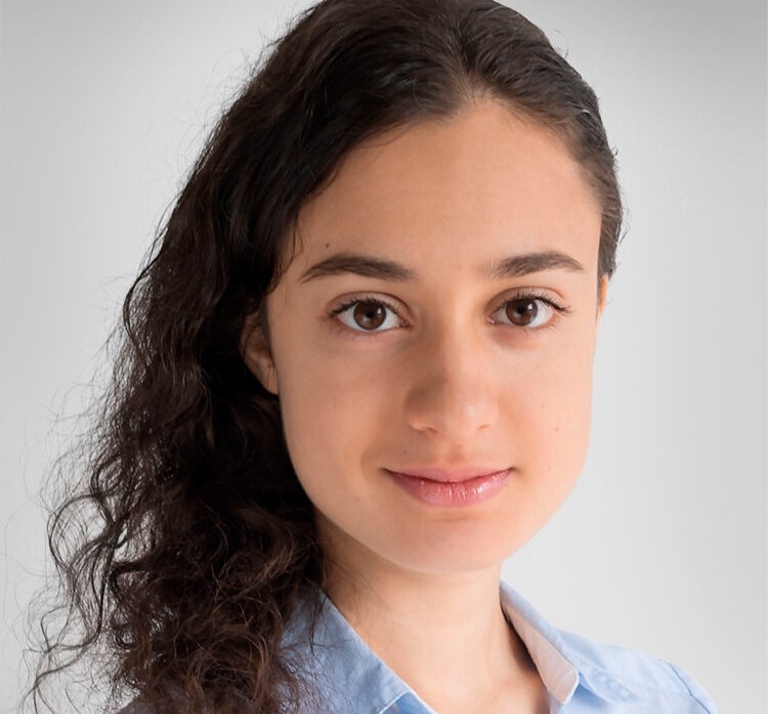 Young woman with dark curly hair and brown eyes wearing blue collared shirt