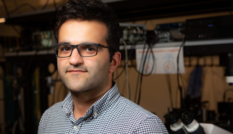 Man with dark hair and glasses standing in a lab