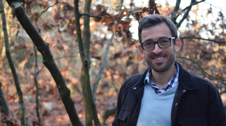 Seth Wynes wears dark jacket and stands in a forested area