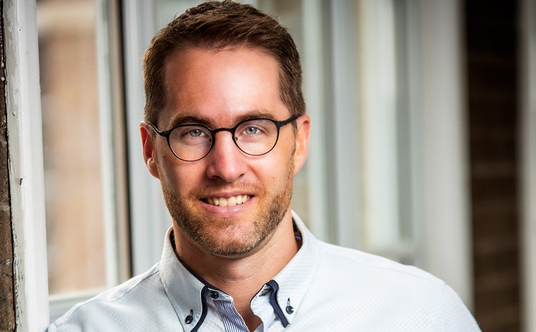 Young, smiling man with blue eyes, short hair, a beard and dark-rimmed glasses.