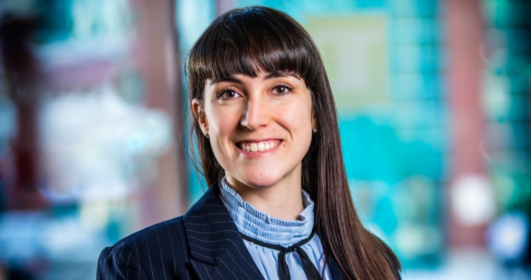 Young, smiling woman with long, dark hair, a blue shirt and navy blue jacket