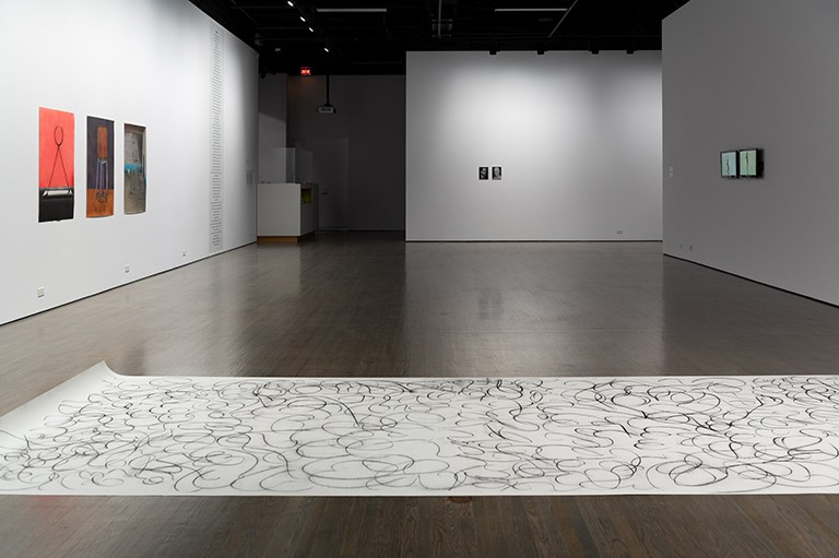 View of an art installation, with images on the sparse white walls.