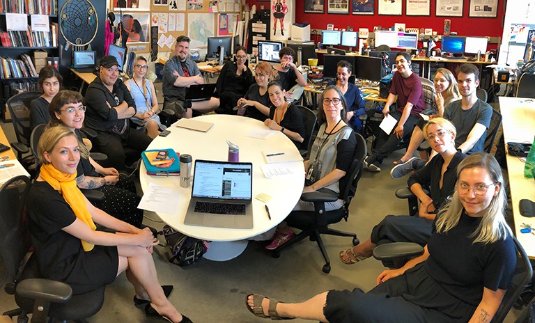 A group of people sitting round a round table in a large office.