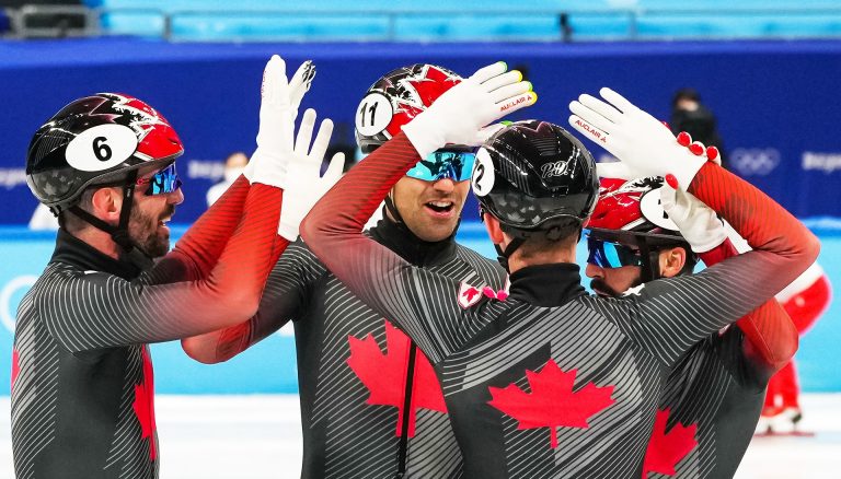 A group of athletes high-fiving at the Olympic Games in grey form-fitting suits embossed with the Canadian Maple Leaf.