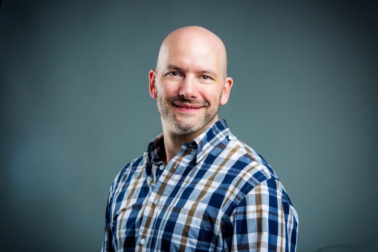 Smiling man wearing blue, white and brown plaid collared shirt