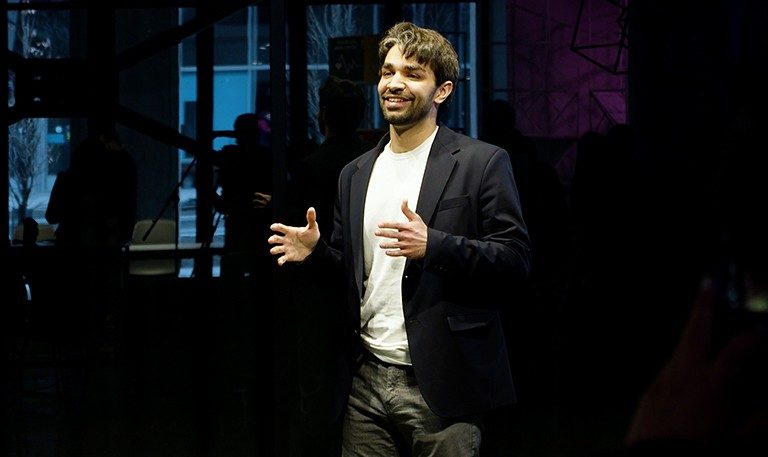 A young man with short dark hair talking to an audience from the stage.